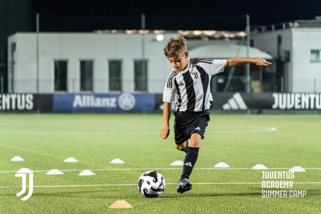 A young boy focuses on his soccer technique during evening training at the Juventus Masterclass Summer Camp in Turin, Italy. Ideal for soccer summer camps and youth summer camp experiences.