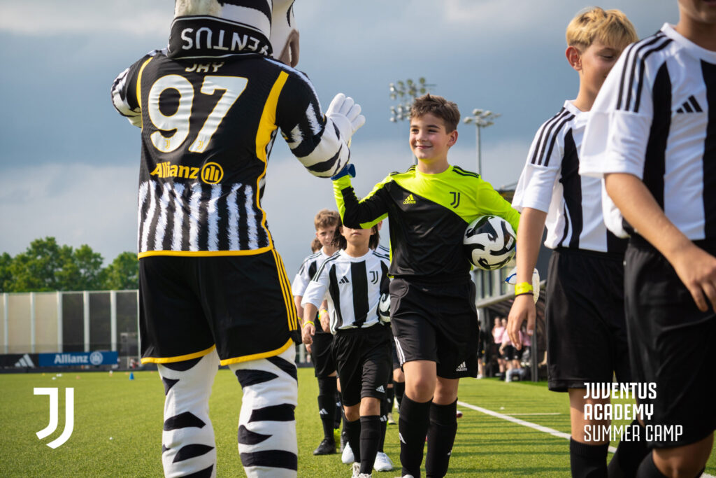 Juventus mascot Jay high-fives young participants at the Juventus Masterclass Summer Camp, promoting summer camps in Italy for youth sports enthusiasts.
