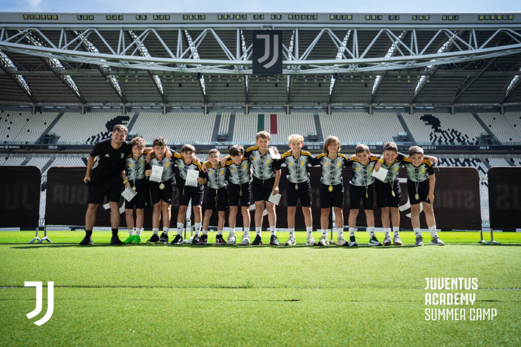 A group of teens proudly pose with medals at the Juventus Stadium during the Juventus Masterclass Summer Camp, experiencing the ultimate soccer camp for youth.