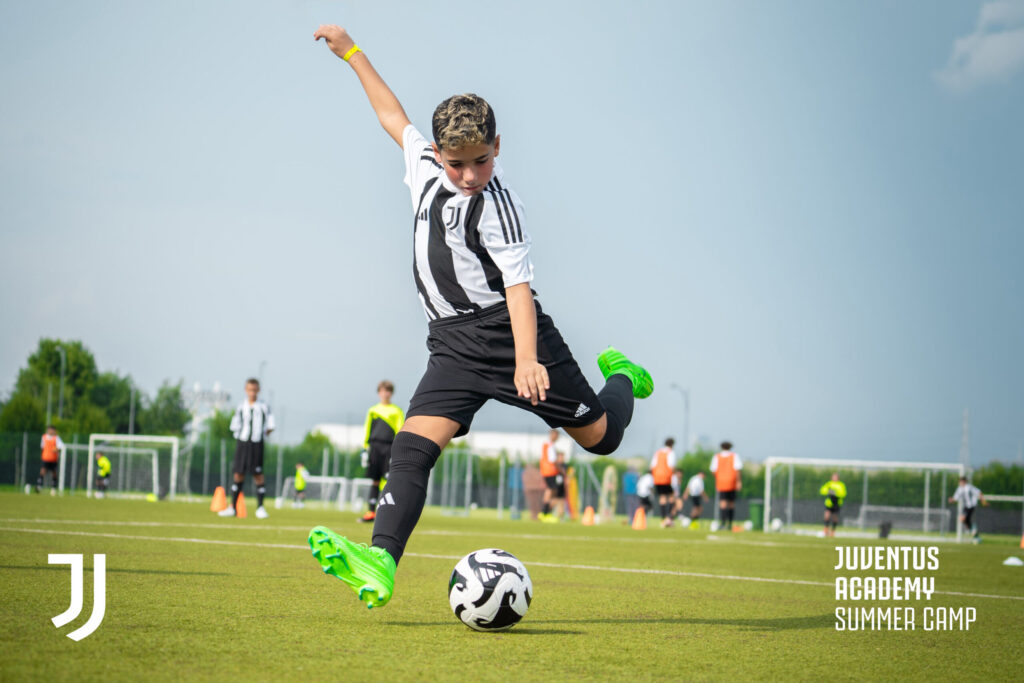 A young boy practices a powerful kick during training at the Juventus Masterclass Summer Camp in Turin, emphasizing soccer skill-building in a summer camp environment.