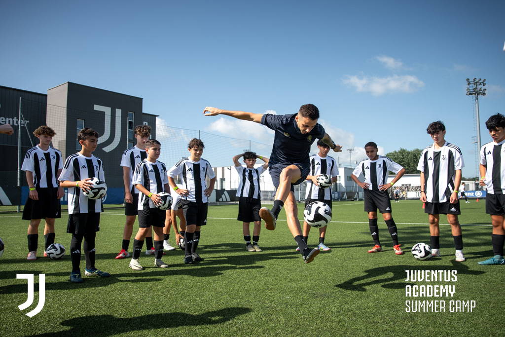 Young soccer players watching freestyle skills demonstration at Juventus summer camp training center with professional instructor performing acrobatic ball control